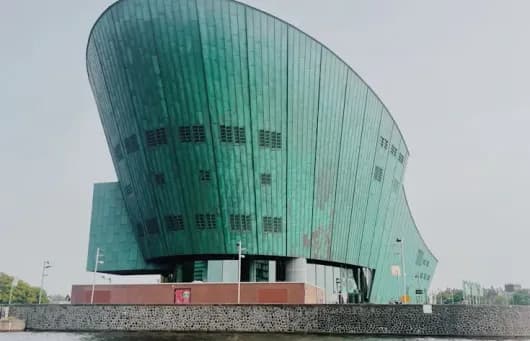 большоее здание в форме носа корабля позвышается над водой